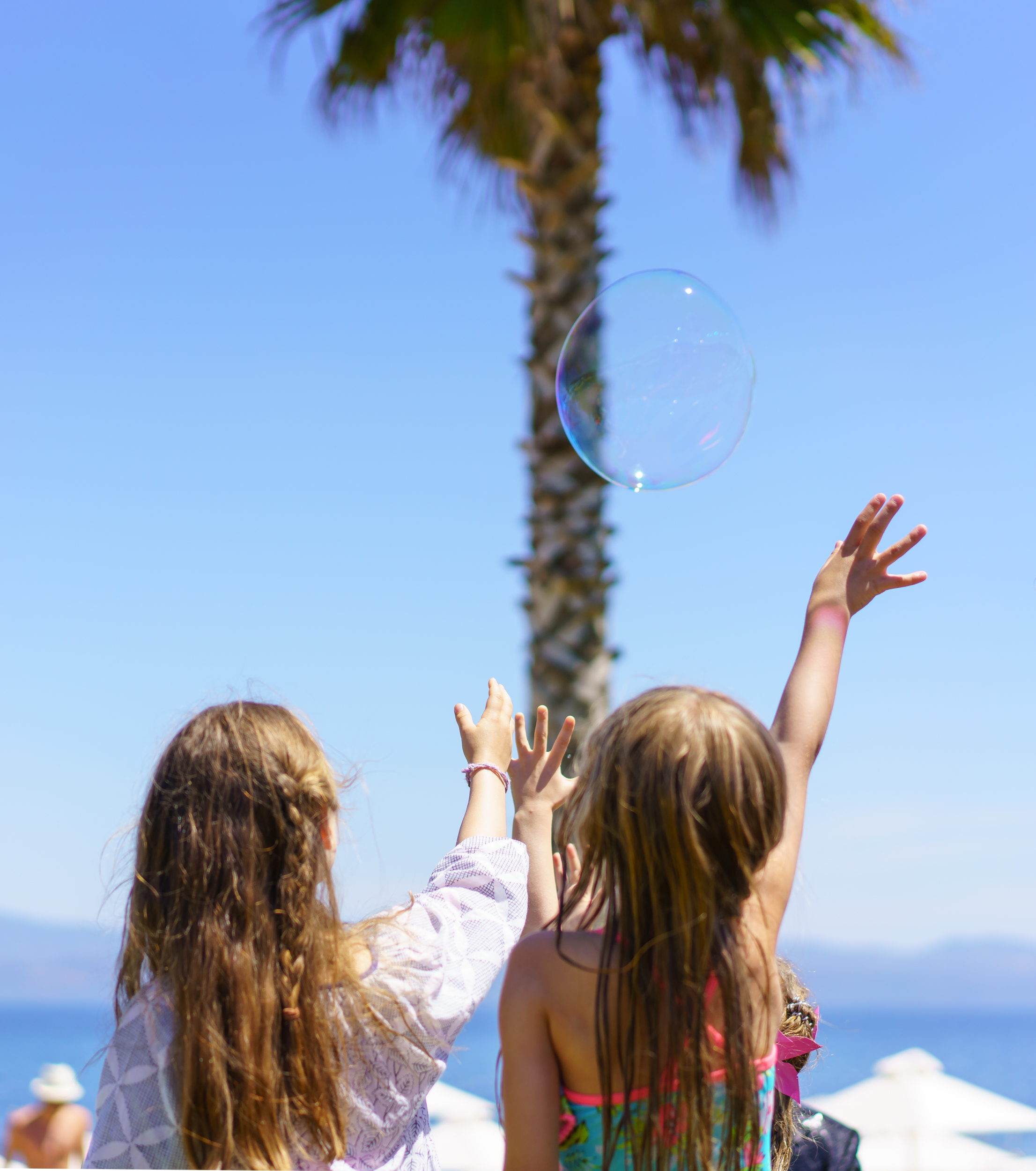 Children playing with a soap bubble near the beach under clear blue sky