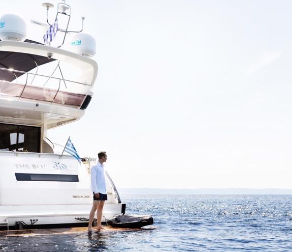 Man standing on the swim platform at the back of a yacht, looking out over the calm open sea