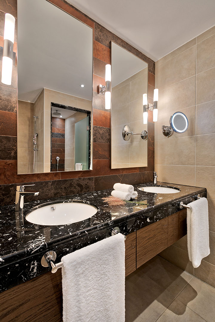 Family garden view room bathroom with marble countertop, dual sinks, and warm lighting