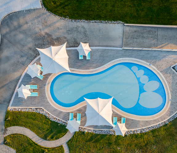 Aerial view of the playful foot-shaped kids' pool with sunbeds and modern white shades surrounded by greenery