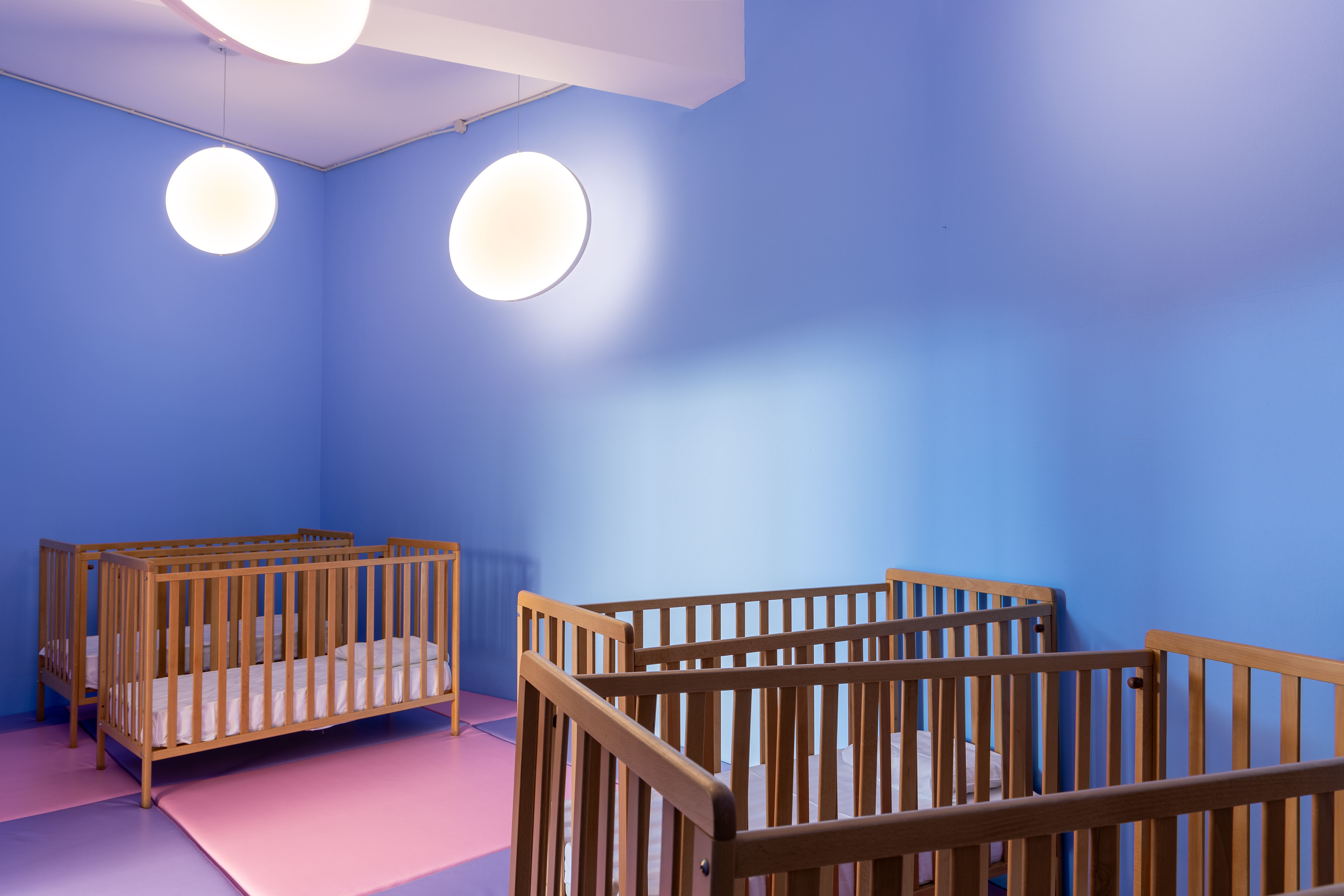 Nursery room with wooden cribs and soft pastel flooring at Kids Planet