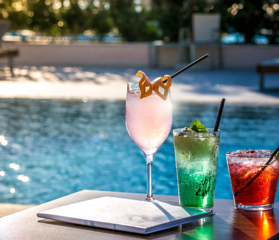 Colorful refreshing cocktails served on the bar counter of Oasis Pool Bar with the pool in the background