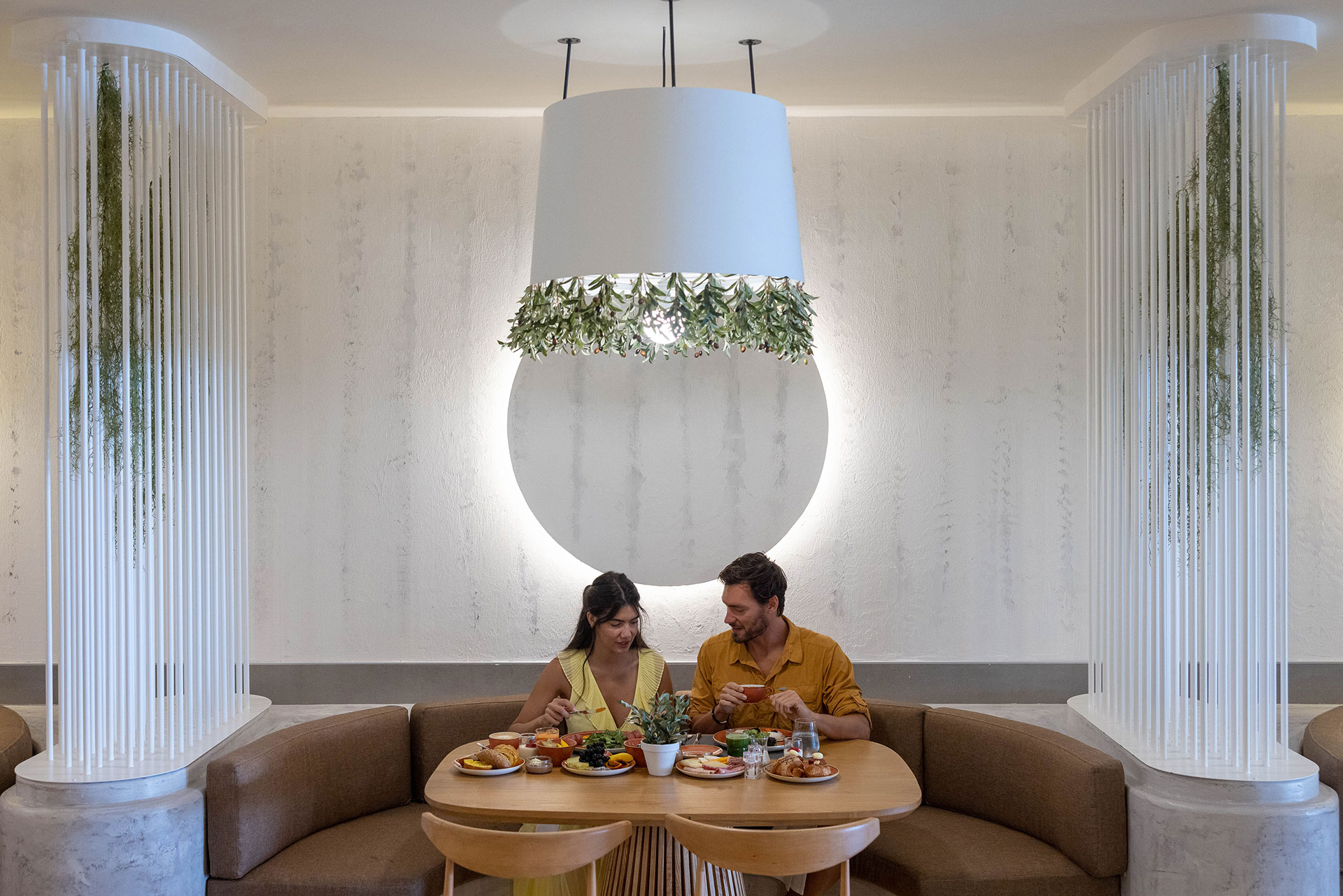 Couple having breakfast under a modern circular light fixture with olive branch decor