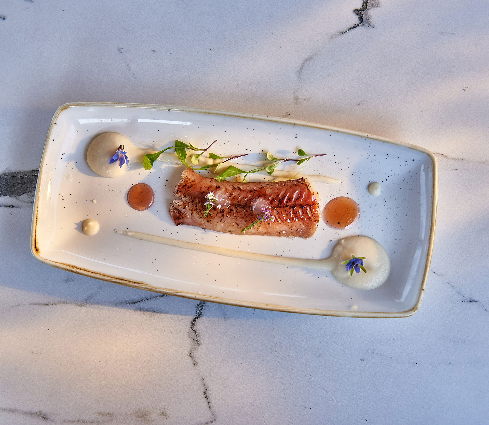 Pan seared red mullet fillet with creamy puree and edible flowers served on marble table