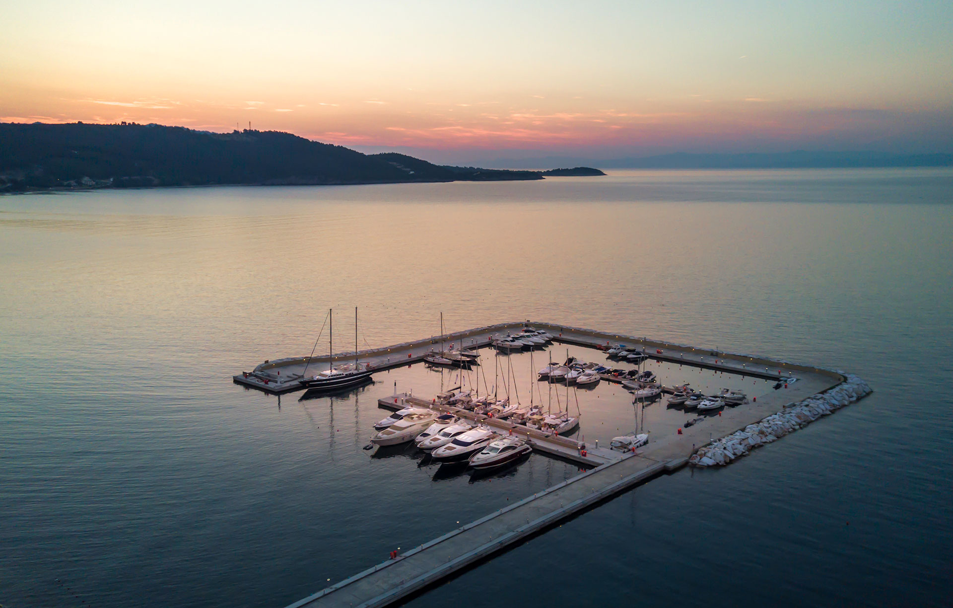 Serene aerial view of yachts anchored at the marina during sunset with calm sea and pastel sky