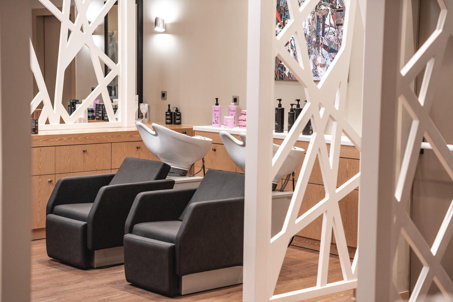 Modern hair salon washing stations with sleek recliner chairs and footrests behind a white partition