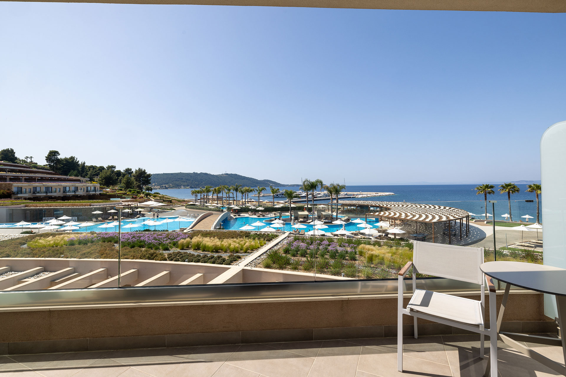 Private balcony view from deluxe room overlooking pools, palm trees, and the Aegean Sea