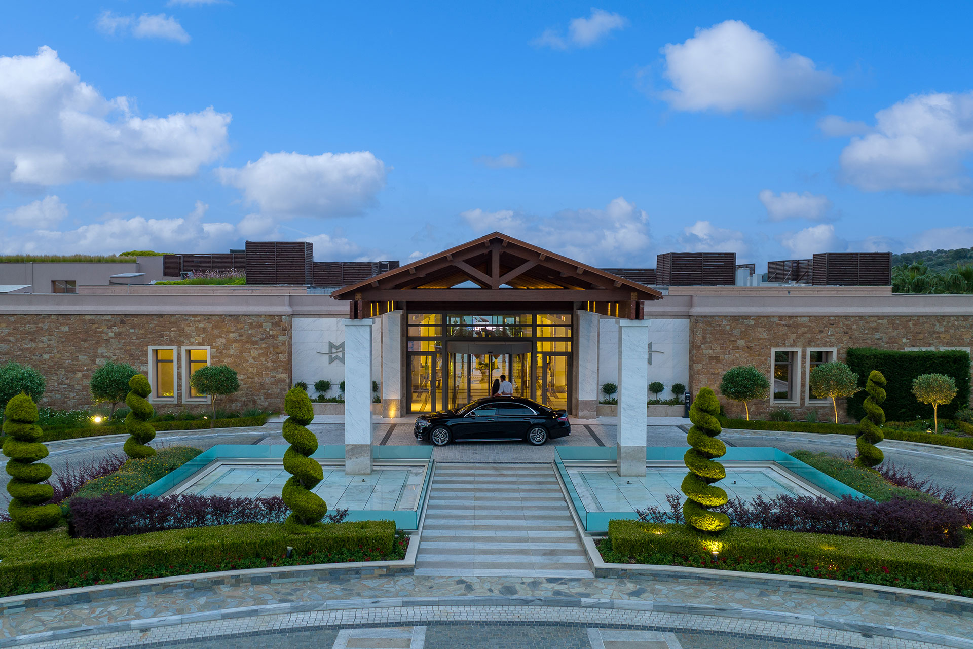 Miraggio Resort's elegant entrance with marble columns, landscaped gardens, and luxury car arrival at dusk