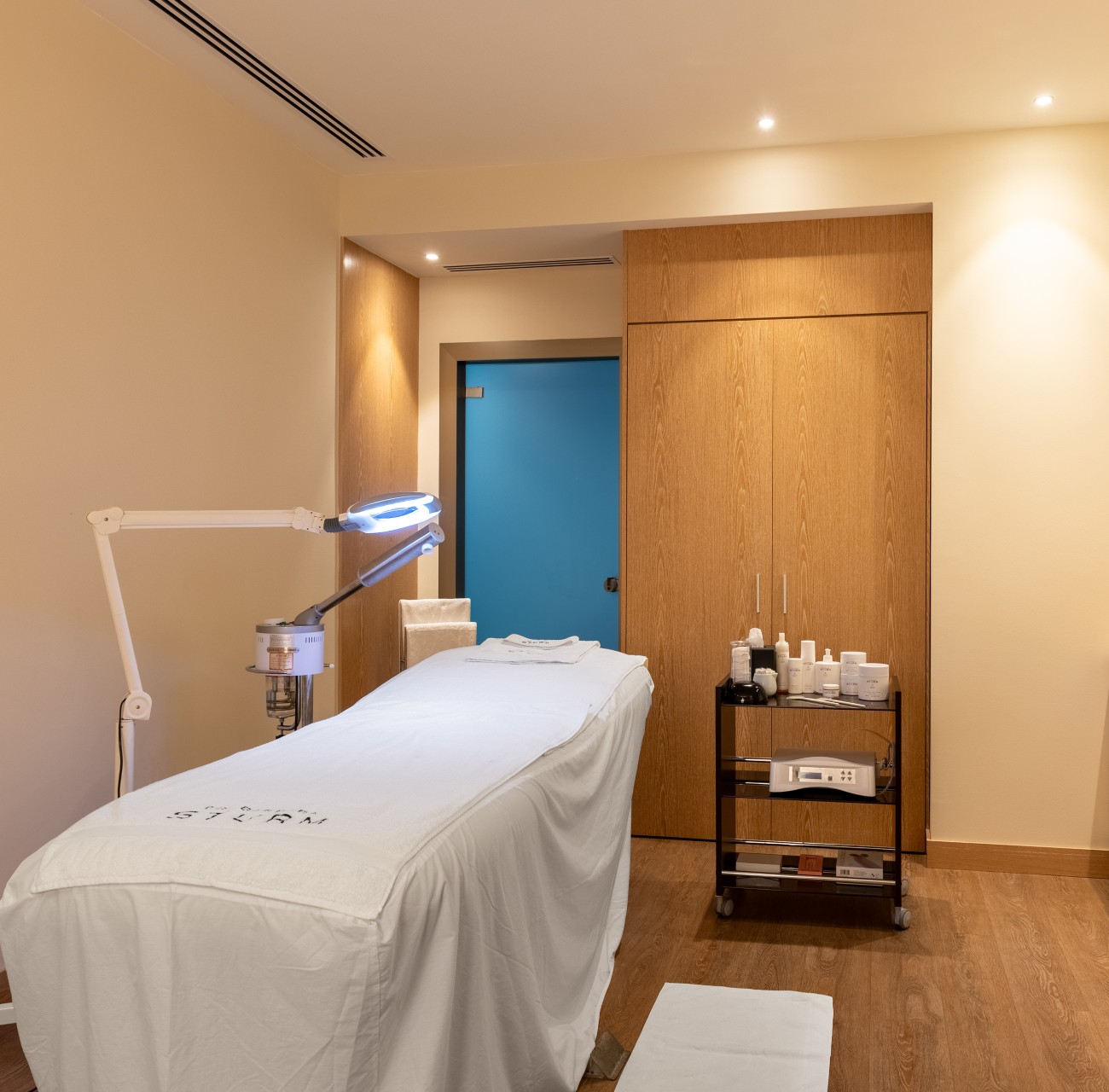 Cozy spa treatment room with a single treatment bed, magnifying lamp and trolley with skincare products