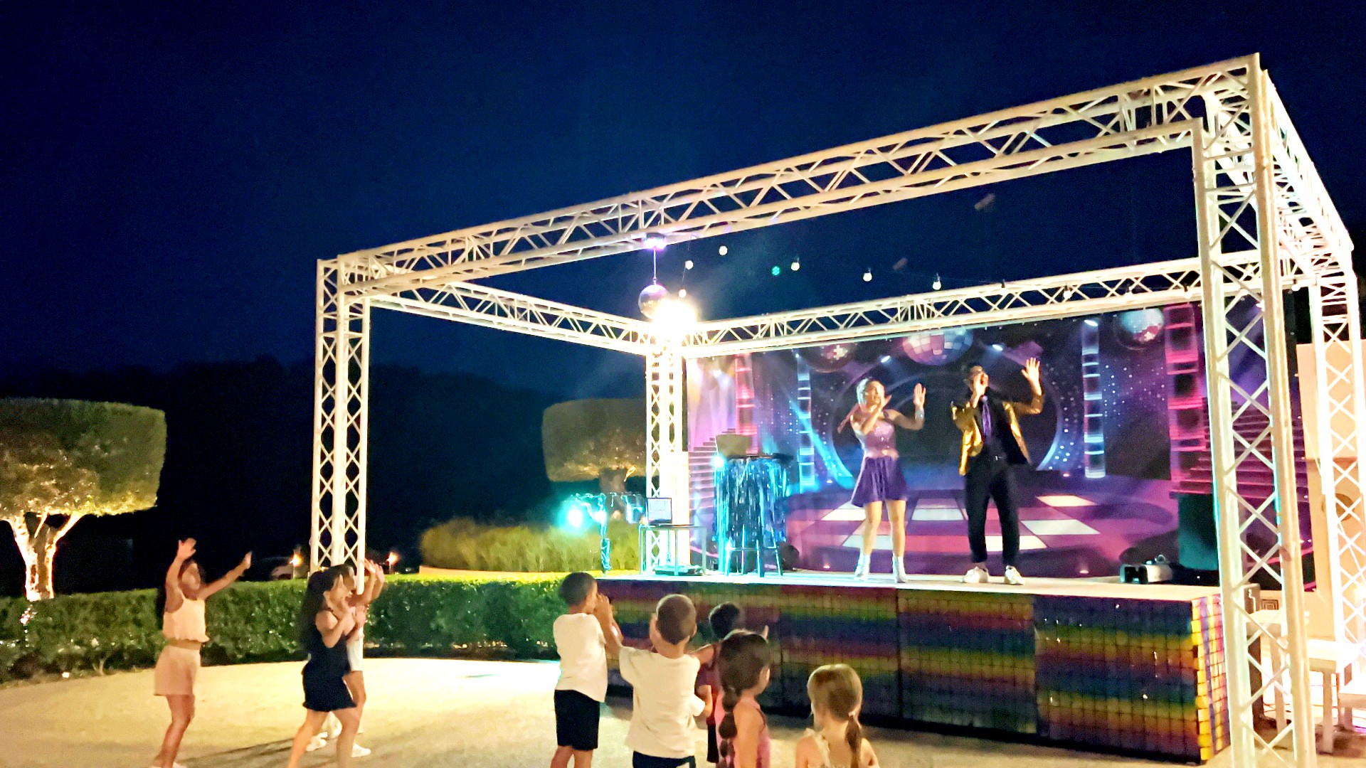 Kids dancing at an outdoor disco performance with colorful light and music