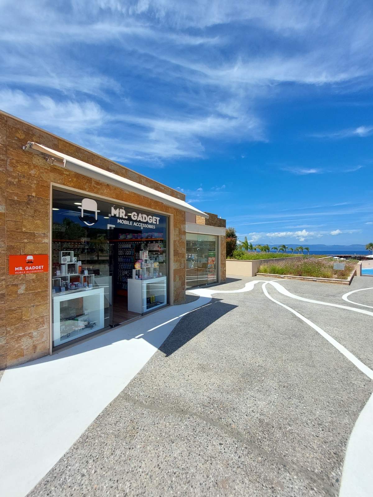 Mr. Gadget store exterior with sea view, palm trees, and clear blue sky