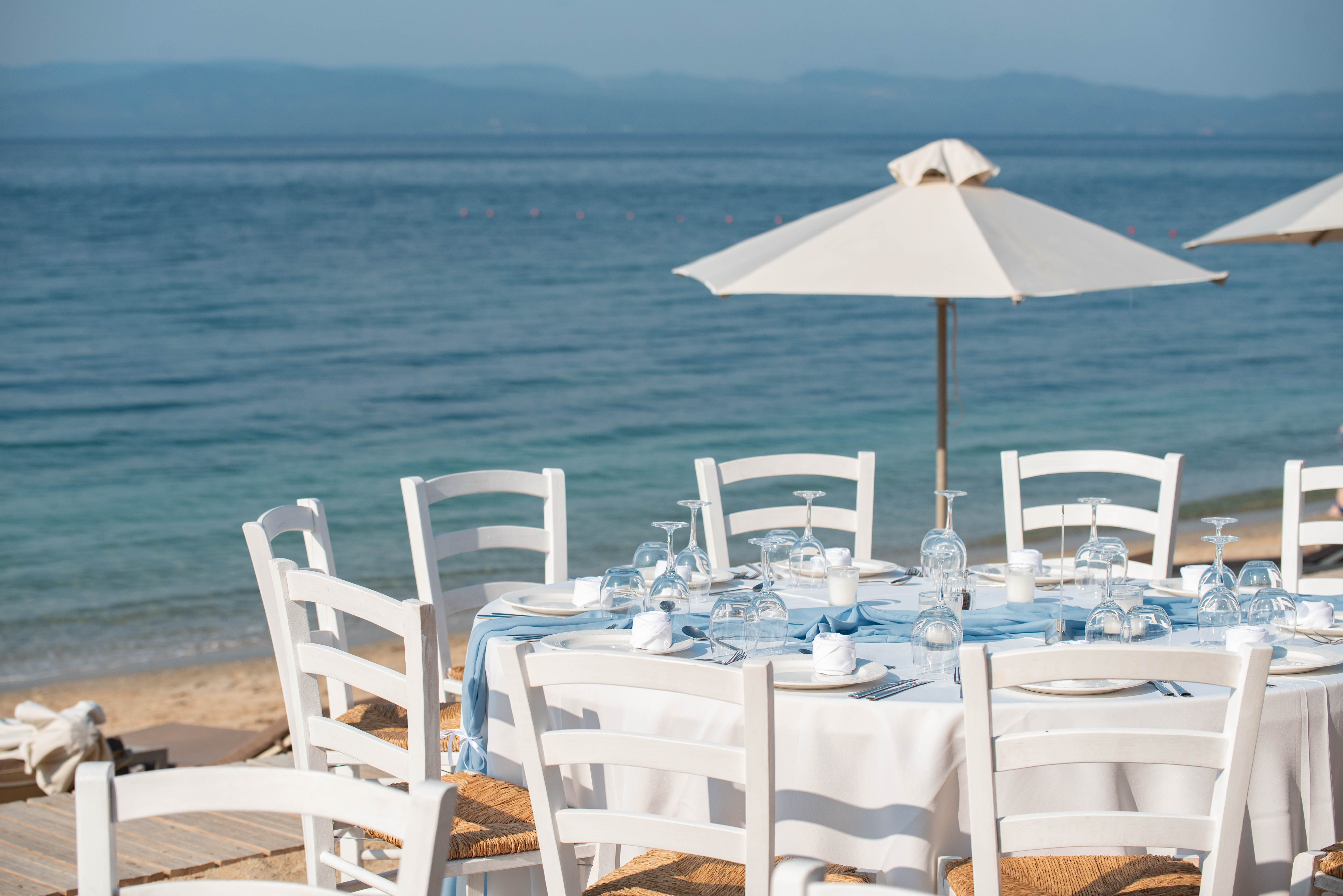 Beach wedding table setup with round tables and rustic chairs facing the sea