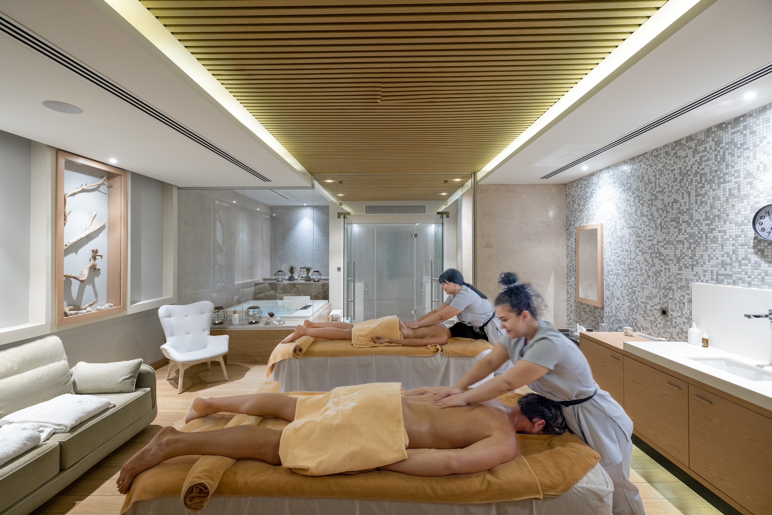 Couple receiving simultaneous relaxing massage from therapists in a candle-li treatment room