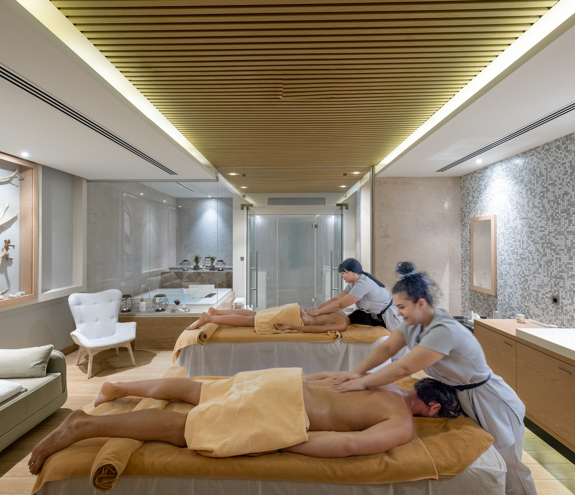 Couple receiving simultaneous relaxing massage from therapists in a candle-li treatment room