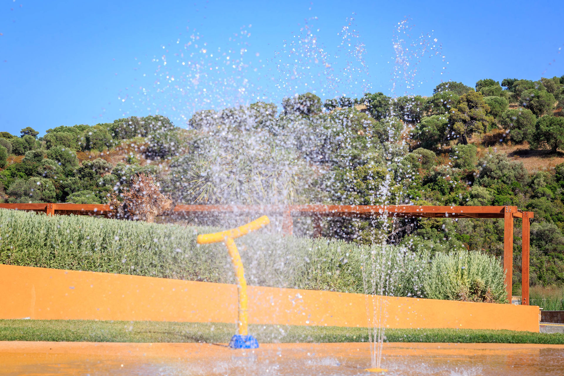 Colorful splash pad with water fountains at Kids Planet, surrounded by greenery and hills