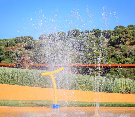 Colorful splash pad with water fountains at Kids Planet, surrounded by greenery and hills