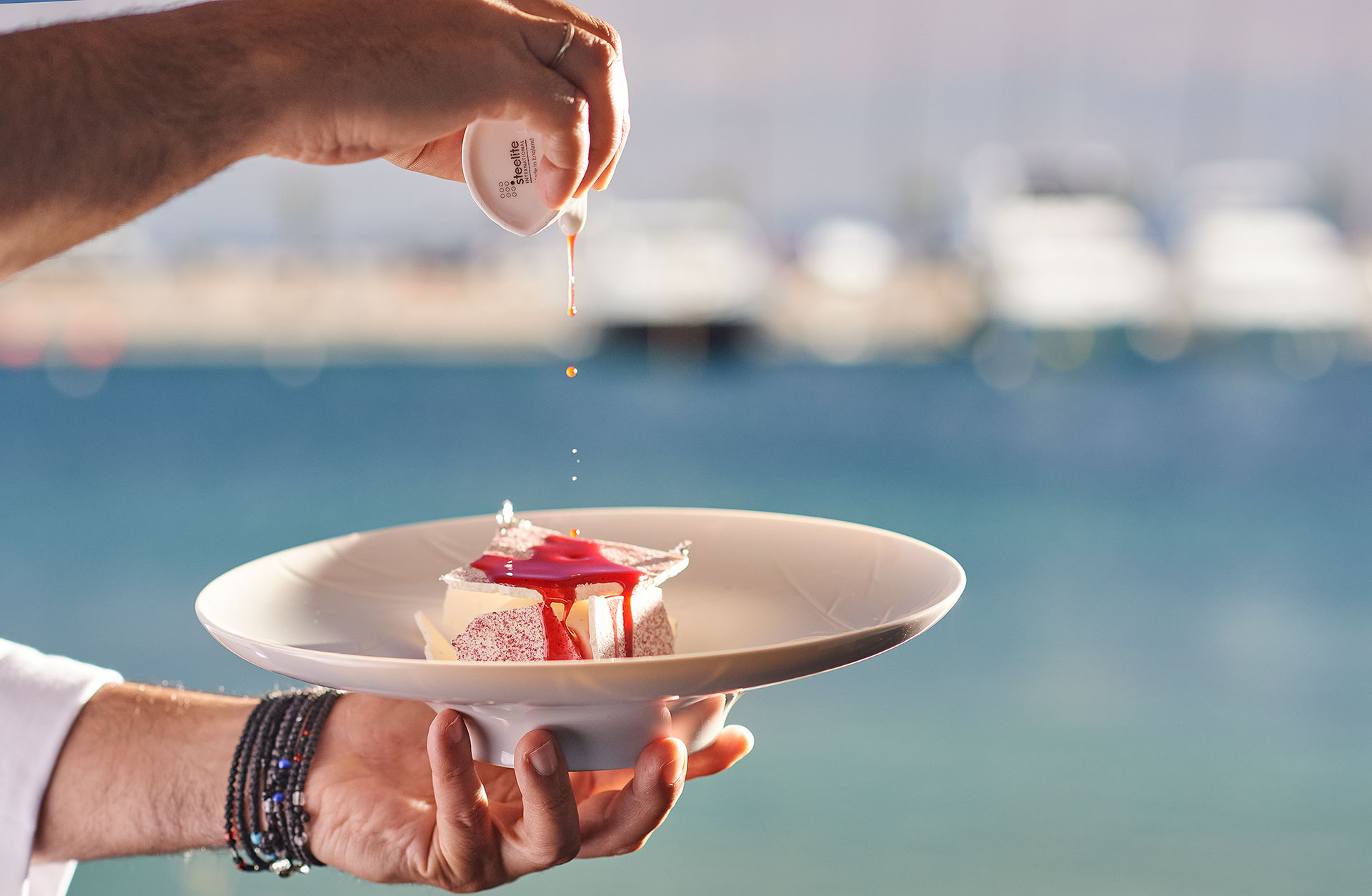 Dessert topped with red sauce being poured by hand against a marina backdrop