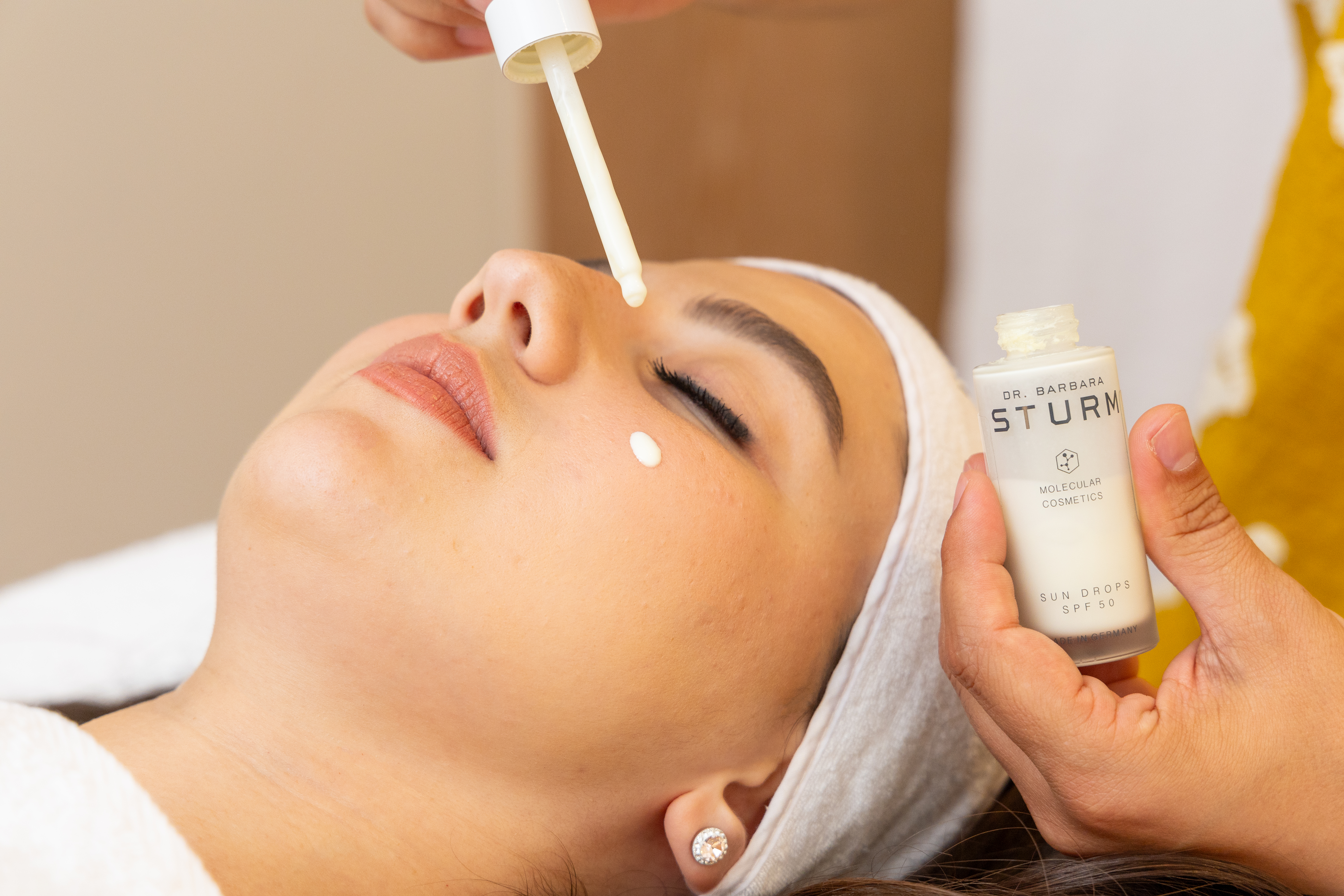 Woman relaxing as spa therapist applies Dr Barbara Sturm skincare products to her face in treatment room