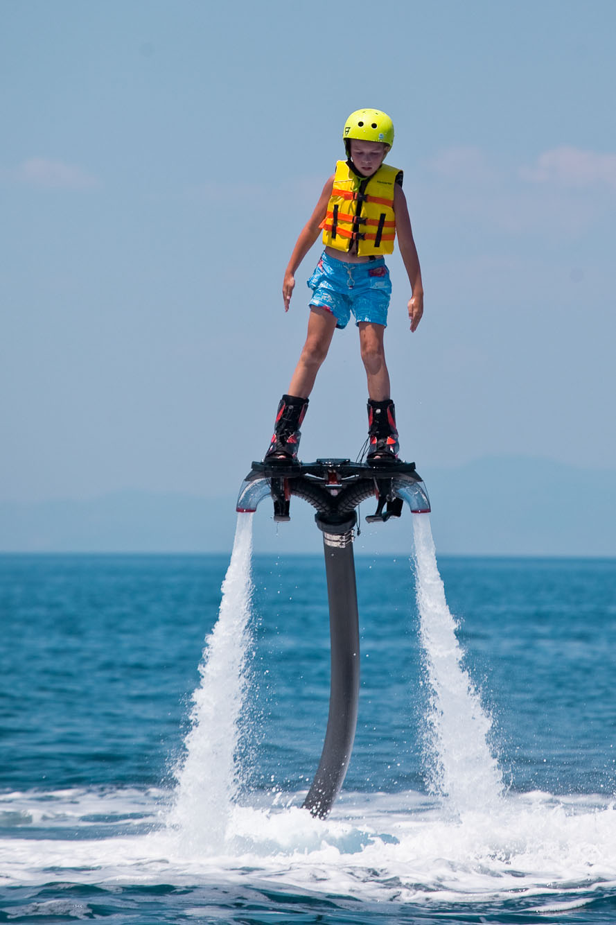 Child riding a flyboard above the sea wearing helmet and life jacket