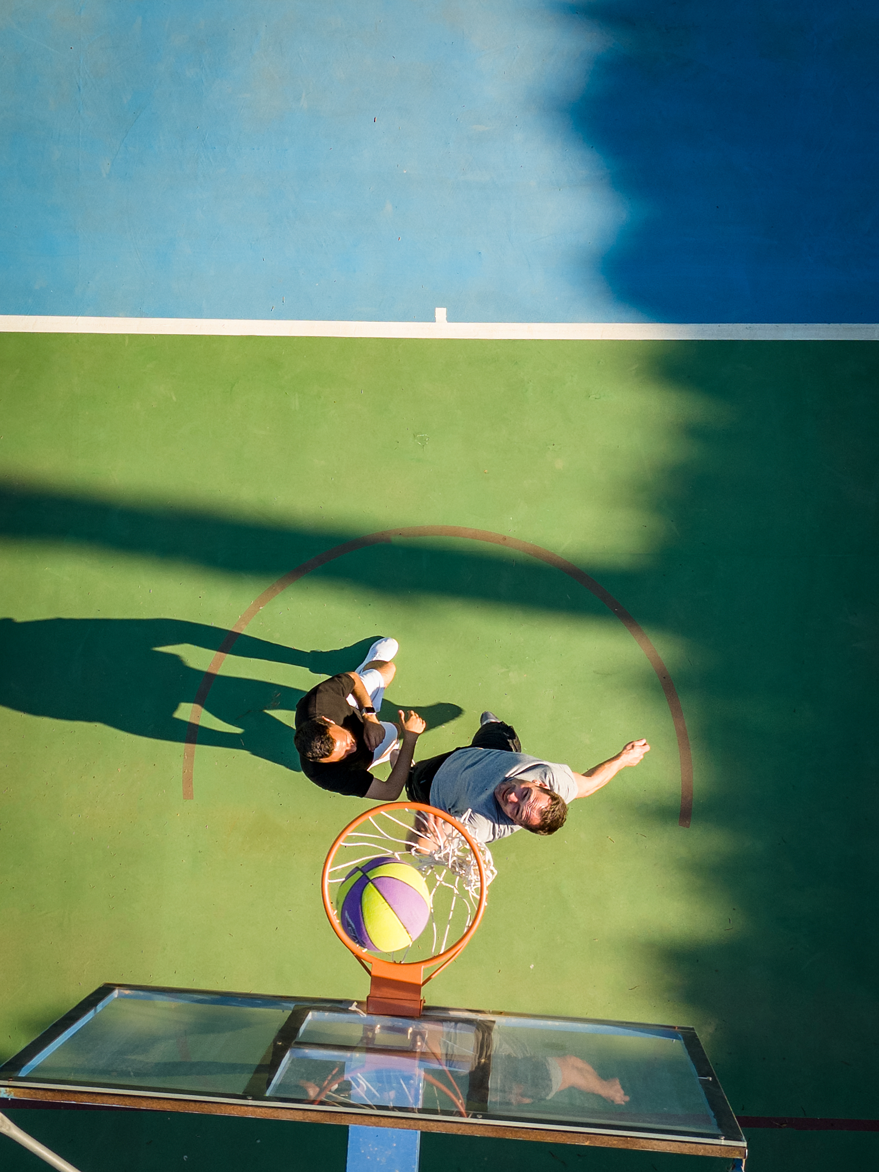 Top down view of basketball court with two players as the ball scores through the hoop