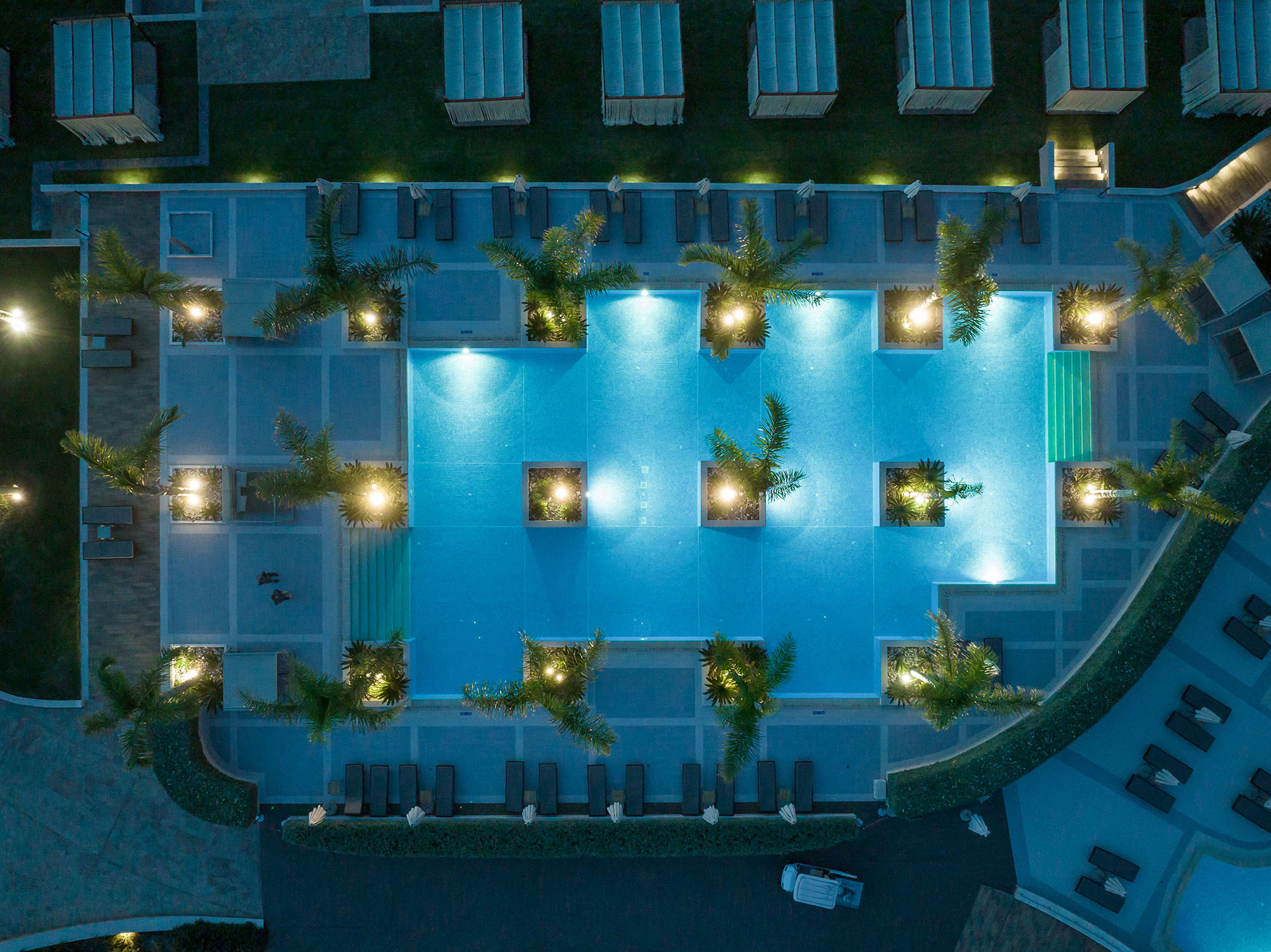 Aerial night view of illuminated main pool with palm trees and cabanas
