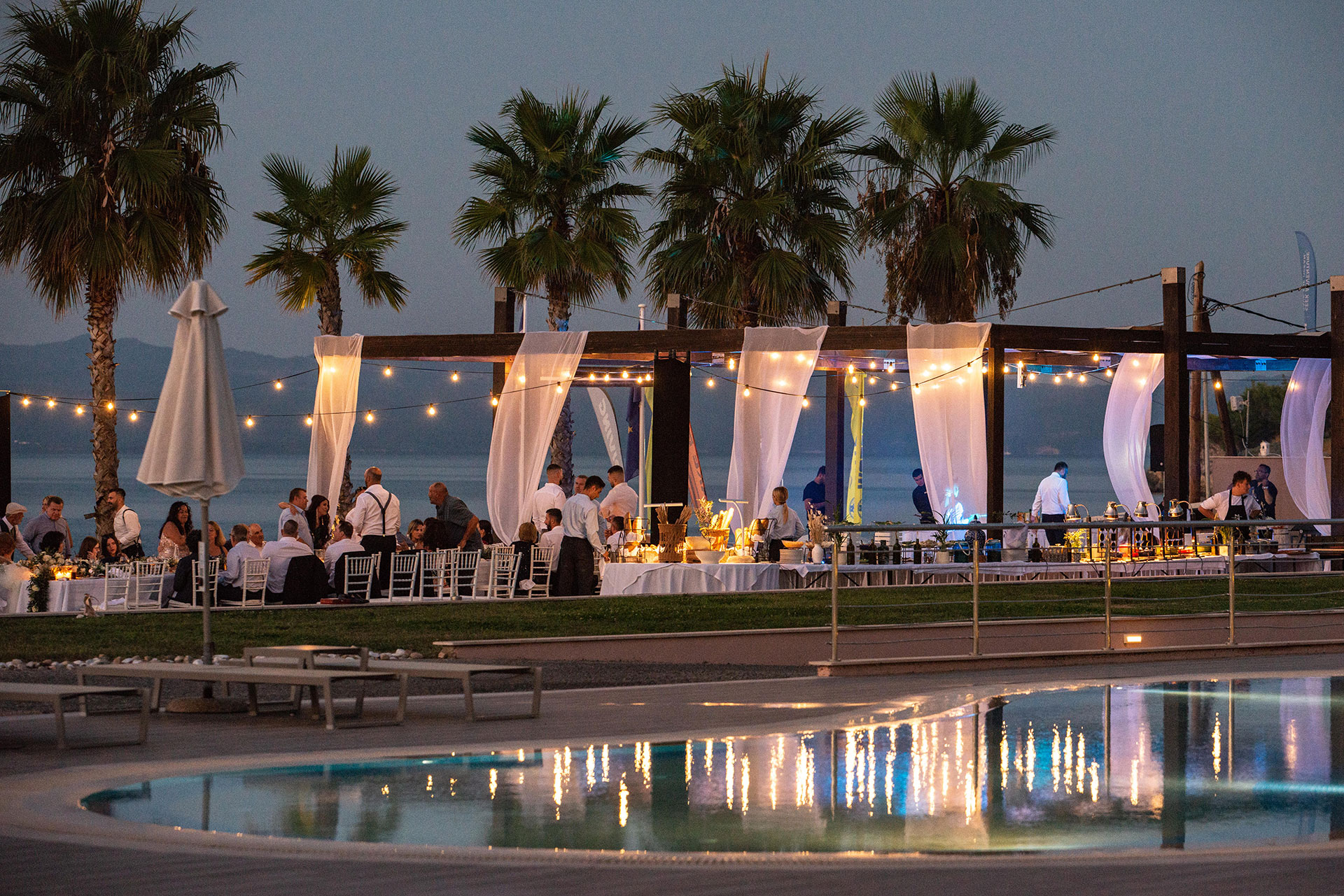 Evening wedding reception by the pool with string lights and palm trees