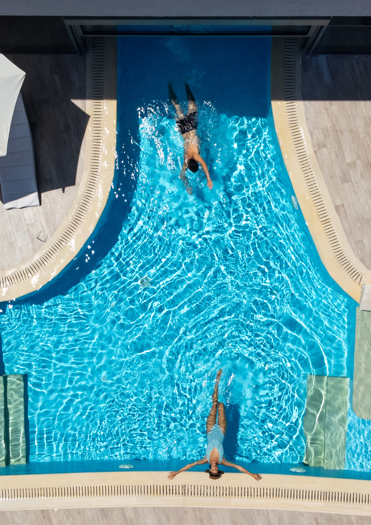 Top down aerial view of crystal clear pool with two guests relaxing in a sunny say
