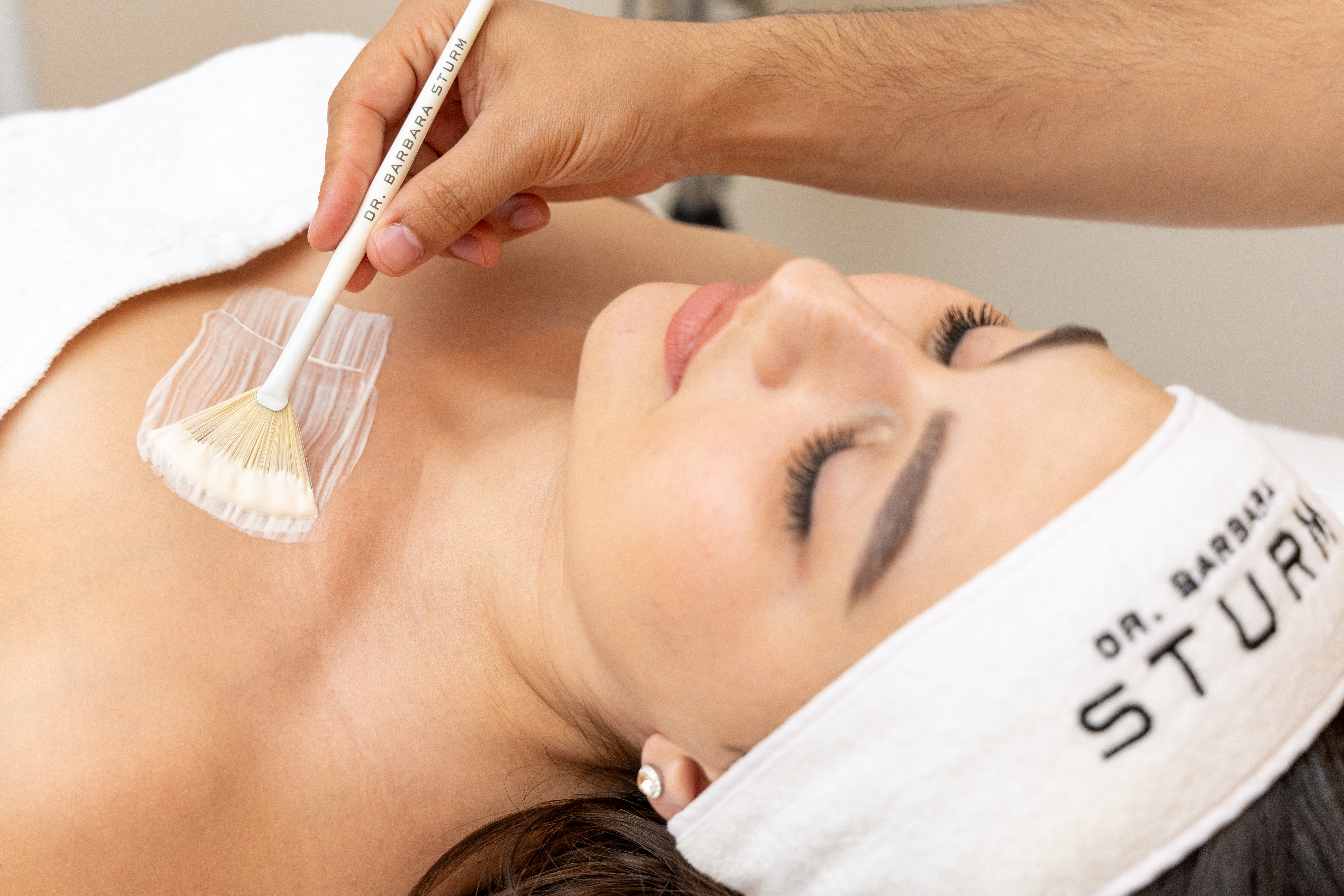Therapist applying premium body treatment with a brush to a woman's chest in a serene treatment room 