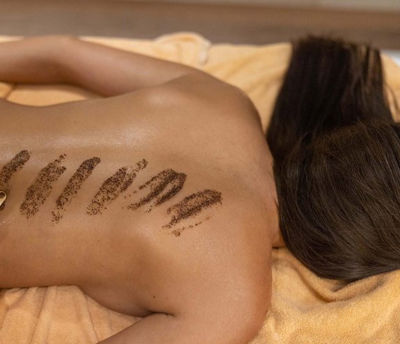 Therapist applying exfoliating body scrub on guest's back during spa treatment