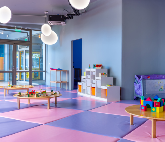 Colorful indoor kids' playroom with activity tables, toys, and soft mats at Kids Planet